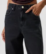 Pantalón wide leg de denim negro, con cintura media, bolsillos funcionales, presillas para cinturón y cierre frontal con botón y cremallera.