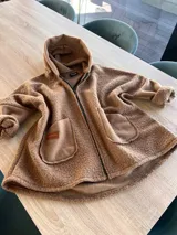 Campera oversize de textura tipo corderito, color marrón, con capucha, cierre frontal completo y dos bolsillos delanteros tipo parche con etiqueta de marca.