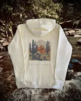 Hoodie oversize color crema con estampado en la espalda que representa un paisaje desértico con cactus y montañas, acompañado por el texto 'DESERT VIBES'.