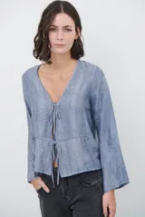 Chaqueta ligera de manga larga en color azul, con escote en V y cierre frontal mediante dos lazos ajustables. Presenta un diseño fluido con textura sutil y corte recto.