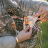 Llavero con cinta de tela estampada de camuflaje y mosquetón de plástico naranja.