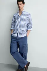 Camisa de corte regular fit confeccionada en tejido de algodón, con diseño de rayas verticales en azul y blanco. Presenta cuello solapa con botones, cierre frontal de botones, manga larga con puños abotonados y un bolsillo en el pecho.