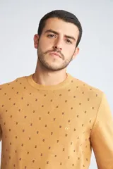 Sweater de punto color mostaza con cuello redondo y mangas largas. Presenta un estampado de pequeños motivos repetidos en contraste y un logo bordado en el pecho.
