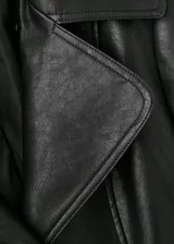 Abrigo largo de estilo trench confeccionado en cuero sintético negro, con diseño recto, cuello con solapa y detalle de cuello de pelo sintético extraíble. Cuenta con cierre frontal de botones, cinturón ajustable con hebilla, bolsillos laterales y mangas largas con trabillas.