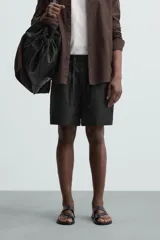 Bermuda de lino color blanco hueso, de corte relajado y tiro medio. Presenta cintura elástica ajustable con cordón, pliegues frontales y bolsillos laterales y trasero.