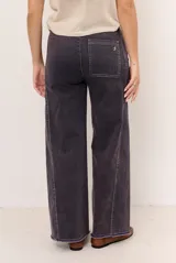 Jean tostado de corte wide leg, tiro medio con presillas y lazo ajustable en la cintura. Presenta bolsillos delanteros y traseros, costuras decorativas verticales y terminación desmechada en el ruedo.
