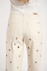 Jean de corte recto y tiro medio, color off-white, con diseño de pequeños bordados en forma de cruz distribuidos por toda la prenda.