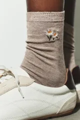 Calcetines de media caña en color beige melange con puntera y talón en contraste color marrón. Presentan un pequeño bordado de flores en la parte superior.