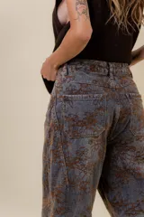 Jean de corte wide leg con estampado floral en tonos tierra sobre base de denim gris oscuro. Presenta tiro medio-alto, bolsillos traseros funcionales y costuras reforzadas.