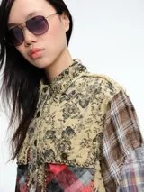 Chaqueta larga tipo camisa con diseño patchwork, confeccionada mediante la combinación de diversos tejidos de algodón con estampados de cuadros, tartán y motivos florales. Presenta cierre frontal con botones, cuello clásico, bolsillos delanteros con solapa y bordes deshilachados.