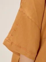 Chaqueta de lino y rayón color tostado, de corte holgado, mangas cortas amplias, cuello mao y cierre frontal oculto con cremallera. Presenta pespuntes a contratono en las costuras y cordón ajustable en el bajo.
