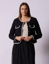 Chaqueta de tweed negra marca Nanette, con escote a la base, abertura central con botones, bolsillos delanteros, aplique de botones perlados en los puños, ribete en contraste blanco y forro interno.