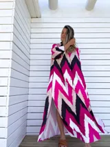 Vestido camisero largo con diseño de estampado chevron en colores fucsia, beige y negro. Presenta cuello camisero, cierre frontal con botones y mangas tres cuartos.