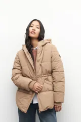 Campera puffer color tostado con capucha, cierre frontal con botones a presión y bolsillos laterales. Presenta diseño acolchado, puños elásticos y ajuste en la cintura.