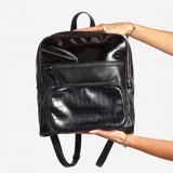 Mochila negra de cuero sintético con textura croco en el bolsillo frontal y parte superior charolada.