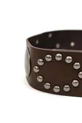 Cinturón marrón de poliuretano ancho, con hebilla metálica plateada, apliques de tachas redondas formando un óvalo decorativo y una placa metálica circular lateral.