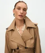 Trench coat largo de Marfinno, confeccionado en gabardina de poliéster. Presenta cuello con solapas, aletas en los hombros, cierre frontal con botones y cinta para lazo en la cintura.