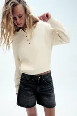 Bermuda de tiro medio confeccionada en denim de color negro gastado, con diseño de cinco bolsillos, trabillas para cinturón y cierre frontal con cremallera y botón metálico.