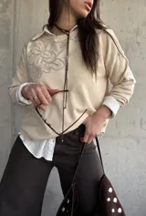 Sweater de punto color beige con bordado floral en el pecho, mangas largas y cuello redondo.