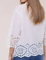Camisa de calce holgado color blanco, confeccionada en tejido liviano de algodón, con cuello camisero clásico, mangas tres cuartos y terminación en puños y ruedo con diseño de bordado broderie calado y festoneado.