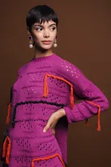Sweater holgado de punto color fucsia, con cuello redondo, manga larga y detalles de bordados a mano con hilo de lurex y flecos naranjas y negros.