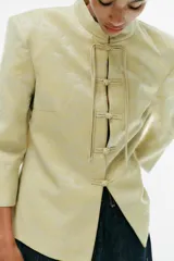 Blazer de jacquard color amarillo claro, con cuello mao, mangas 3/4 y cierre frontal con alamares. Presenta diseño estampado de inspiración oriental.