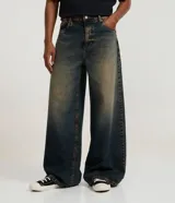 Pantalón mega baggy de corte holgado, confeccionado en jean gris con efecto deslavado. Presenta cintura con trabillas y diseño de tiro medio.