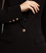 Blazer de sastrería en crepé color negro, con cuello solapa, cierre frontal de un solo botón dorado y bolsillos laterales con solapa.