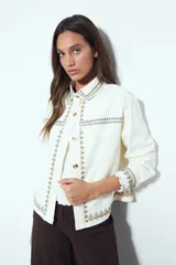 Campera de jean color blanco con bordados geométricos en cuello, delantero, bolsillos, puños y ruedo. Tiene botones dorados y un calce recto y relajado.