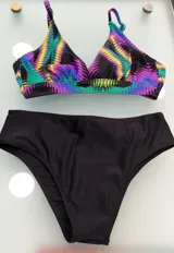 Conjunto de bikini con corpiño de triángulo sin aro, con estampado geométrico vibrante en tonos neón sobre fondo negro, y breteles ajustables. La parte inferior es una bombacha clásica de tiro alto, color negro liso.