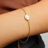 Pulsera dorada de cadena fina con dije ovalado blanco con el símbolo de Aries.