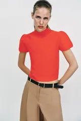 Top de punto color blanco, de cuello redondo y manga corta abullonada.