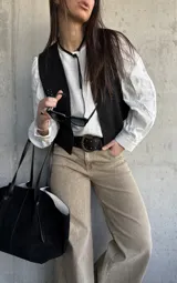 Chaleco negro de gamuza sintética, de estilo boho-chic, con costuras decorativas en los bordes y diseño clásico atemporal.