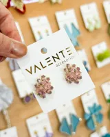 Aretes tipo stud con forma de flor, engastados con circones de tonos rosados y malvas, en base metálica dorada.