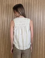 Musculosa de lino color blanco, de corte holgado, con cuello en V, detalles de tablas y frunces en los hombros, y dobladillo desflecado.