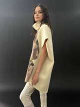Poncho de lana merino afieltrada con cuello alto y mangas cortas. Diseño tipo mosaico con piezas geométricas en tonos verde azulado y gris.