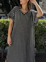 Vestido largo de tejido de punto con diseño de rayas verticales en blanco y negro. Presenta escote en V, mangas cortas y tajos laterales en el ruedo para mayor movimiento.