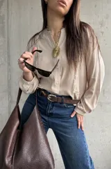 Camisa beige de manga larga con detalles de vainica vertical en el frente y cierre frontal de botones.