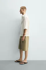 Camisa de corte relajado y boxy fit, confeccionada en tejido con textura irregular. Presenta cuello solapa, manga corta y cierre frontal con botones.