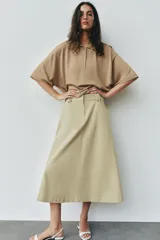 Falda midi de tiro alto color beige, con bolsillos delanteros, cintura con trabillas y cierre frontal con cremallera y ganchos metálicos.