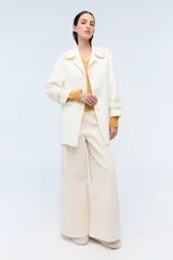 Tapado color crema con cuello solapa, cierre con botones y bolsillos laterales. Presenta detalle de costuras en contraste en cuello, puños y solapa.