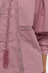 Blusa de algodón liviano color blanco, con detalles de puntilla en el frente, cuello mao con escote en V, cordón colgante y mangas largas abullonadas con puños ajustados.