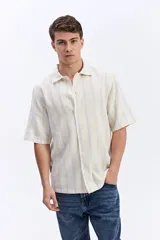 Camisa de manga corta oversize en tejido rústico, con diseño de rayas verticales celestes y blancas, cuello clásico y cierre frontal de botones.