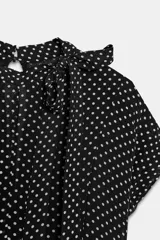 Vestido midi de viscosa con estampado de lunares blancos sobre fondo negro. Presenta cuello redondo con detalle de lazada, manga corta y pliegues en la cintura con bajo recto.