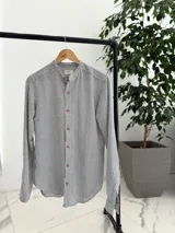 Camisa de lino a rayas verticales grises y blancas, con cuello mao y cierre frontal de botones marrones.