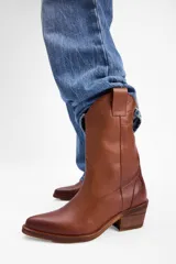 Bota estilo western de caña media, confeccionada en gamuza color marrón con bordados decorativos en hilo claro. Cuenta con taco cuadrado de madera y tiradores laterales.