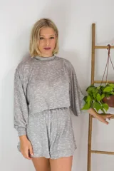 Conjunto de dos piezas en color crema, compuesto por un buzo de cuello alto, mangas largas abullonadas y ajuste en la cintura, junto con un short de tiro alto con terminaciones al corte.