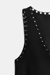 Chaleco negro de escote en pico y manga sisa, con detalle de tachas metálicas en el borde y bajo acabado en flecos largos. Presenta cierre frontal con lazada.