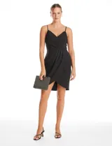 Vestido corto de crepe color negro con escote en V cruzado y drapeado en el busto. Presenta una falda envolvente con diseño drapeado y abertura asimétrica en el bajo, con cierre invisible en la espalda y forro interno.