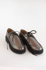 Zapatos tipo wallabee de cuero metalizado en tono peltre, con cordones negros y suela track de goma negra con plataforma.
